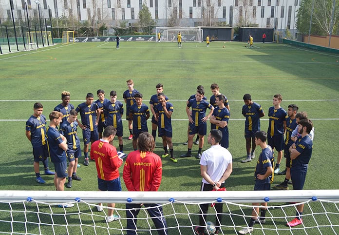 players in blue surround coach for discussion