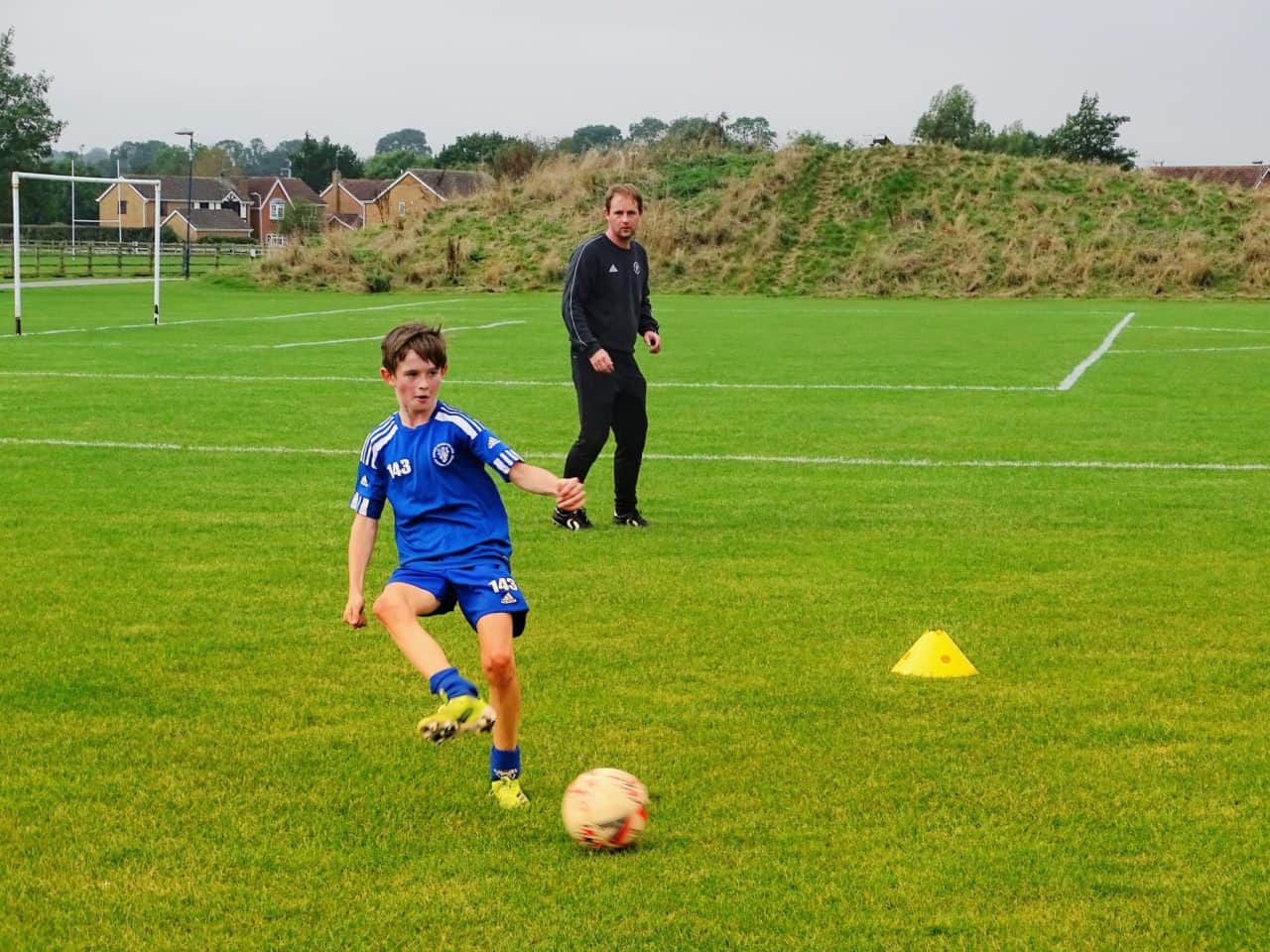 coach watching the kid kick the ball